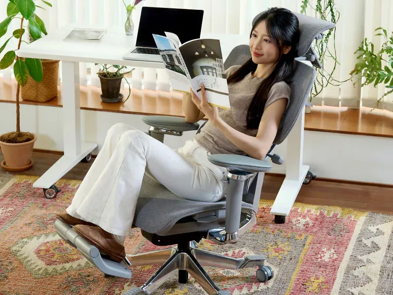 Femme allongée lisant un magazine, jambes posées sur le repose-pied déployé de la FlexiSpot C7 Morpher