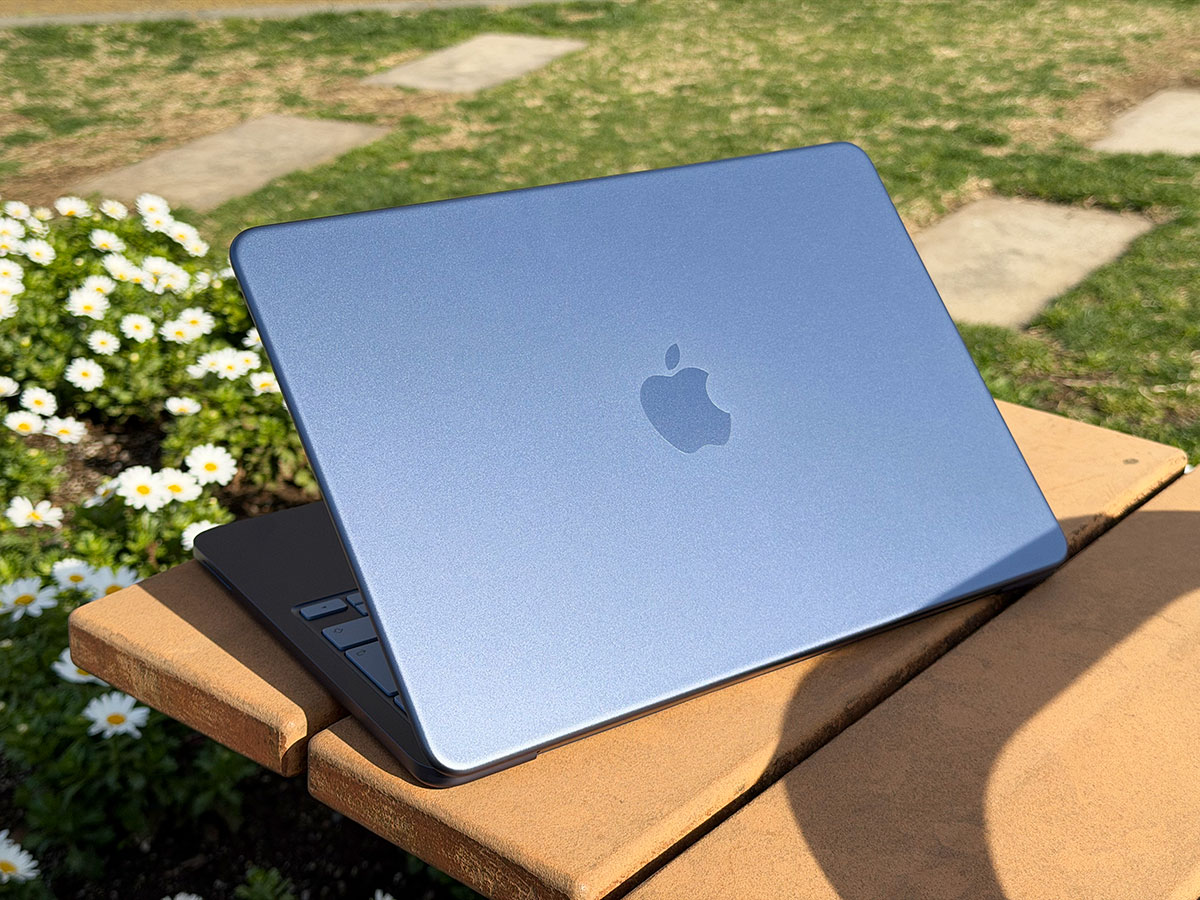 MacBook Neo indigo fermé, posé en extérieur sur un banc