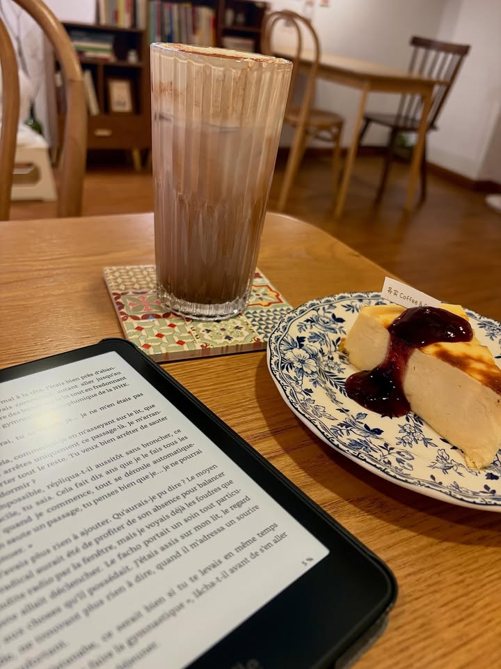 Kindle Paperwhite en lecture dans un café, à côté d'un chocolat chaud et d'un cheesecake