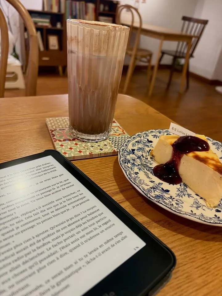 Kindle Paperwhite en lecture dans un café, à côté d'un chocolat chaud et d'un cheesecake
