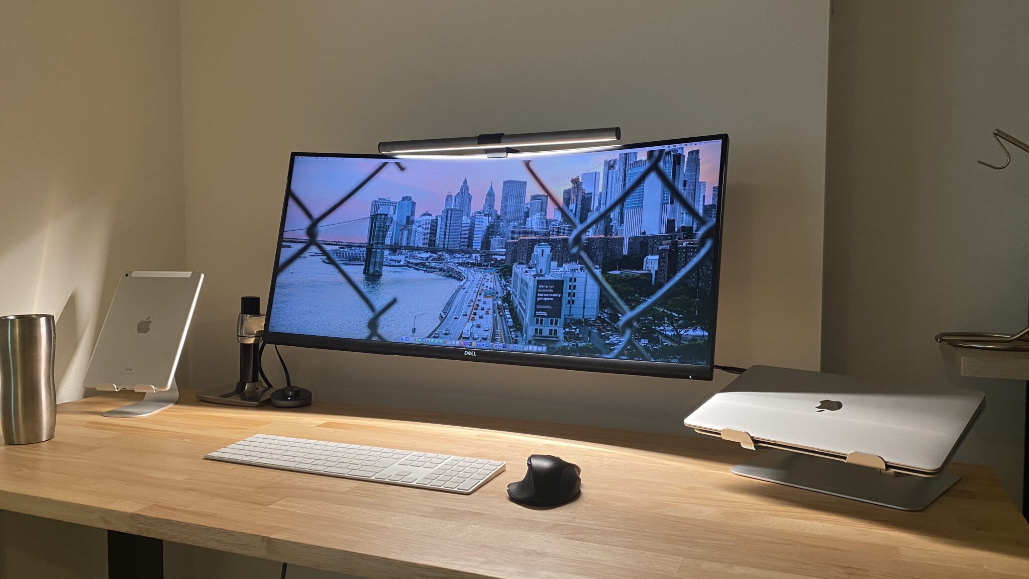 Bureau en bois avec écran ultrawide incurvé sur bras articulé, MacBook sur support, iPad et clavier sans fil