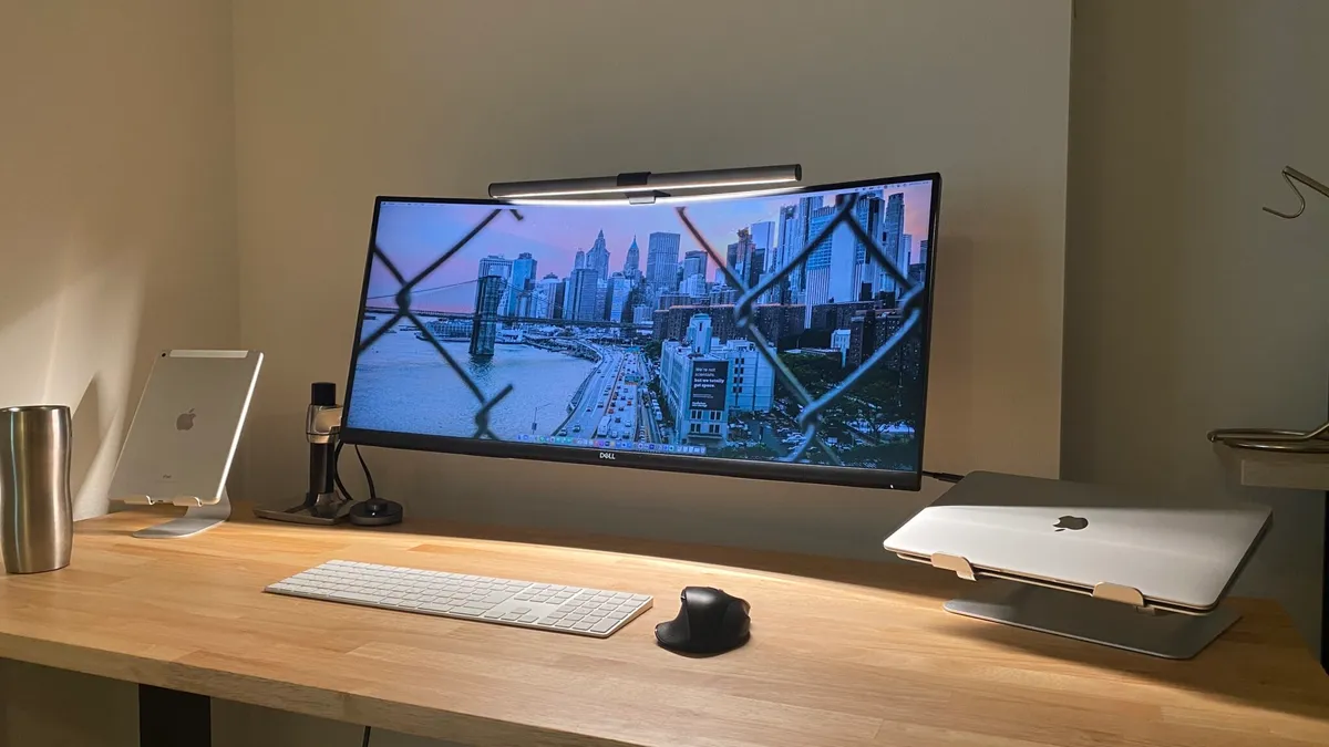 Bureau en bois avec écran ultrawide incurvé sur bras articulé, MacBook sur support, iPad et clavier sans fil