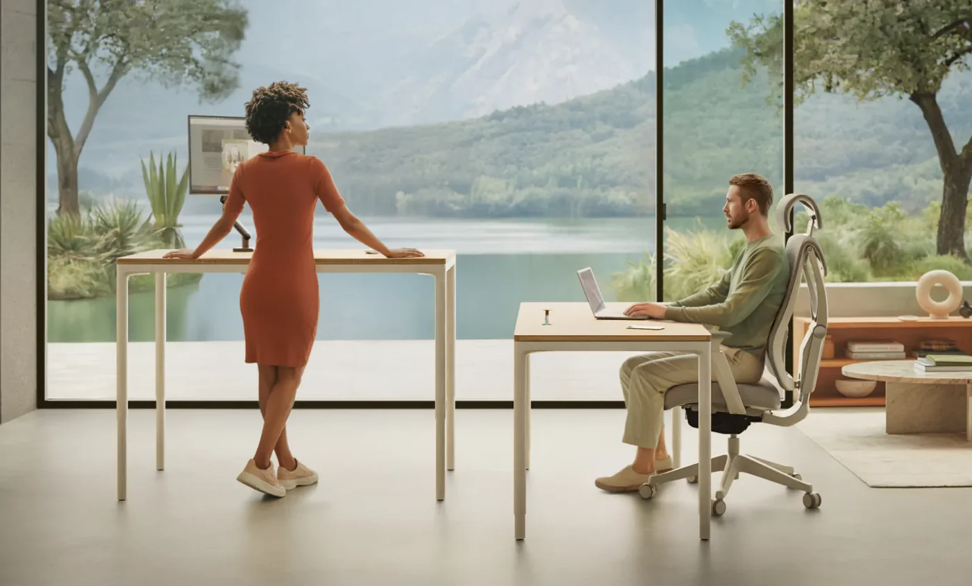 Bureau Desktronic HomeMax en position debout à côté d'un modèle en position assise, face à un lac