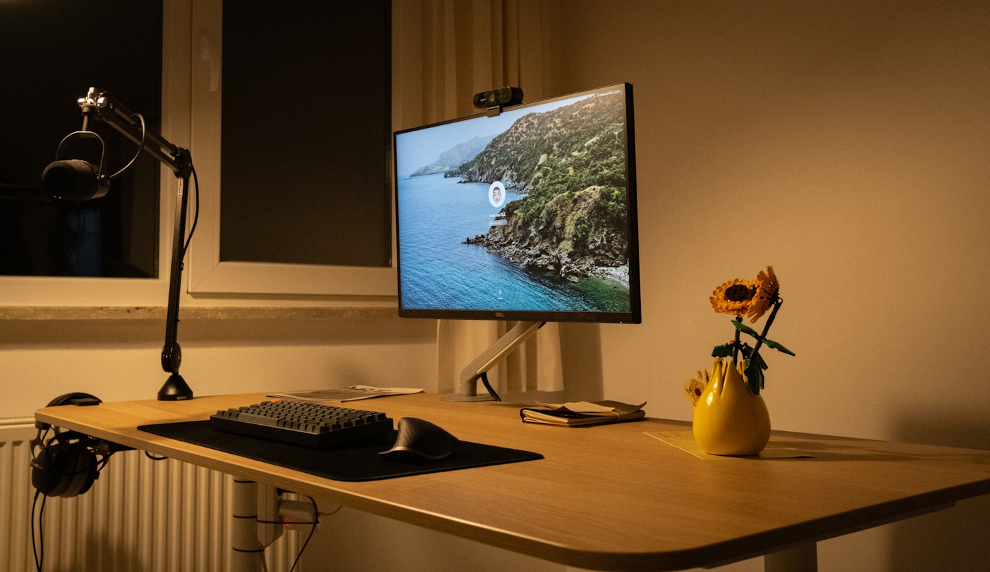 Écran monté sur un bras articulé au-dessus d'un bureau en bois, à la lumière du soir