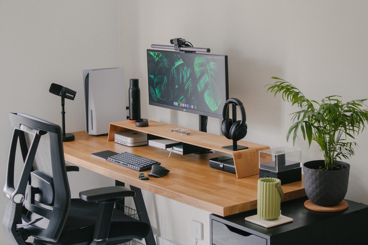 Écran sur rehausseur en bois avec console, casque et clavier sur un bureau clair
