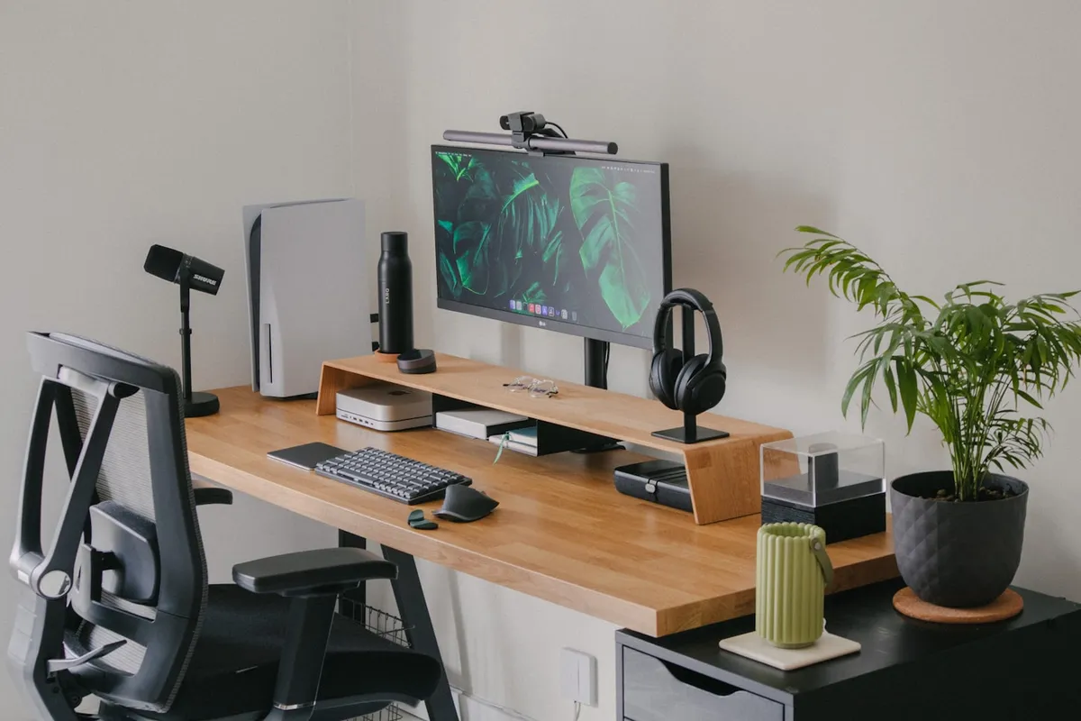 Écran sur rehausseur en bois avec console, casque et clavier sur un bureau clair