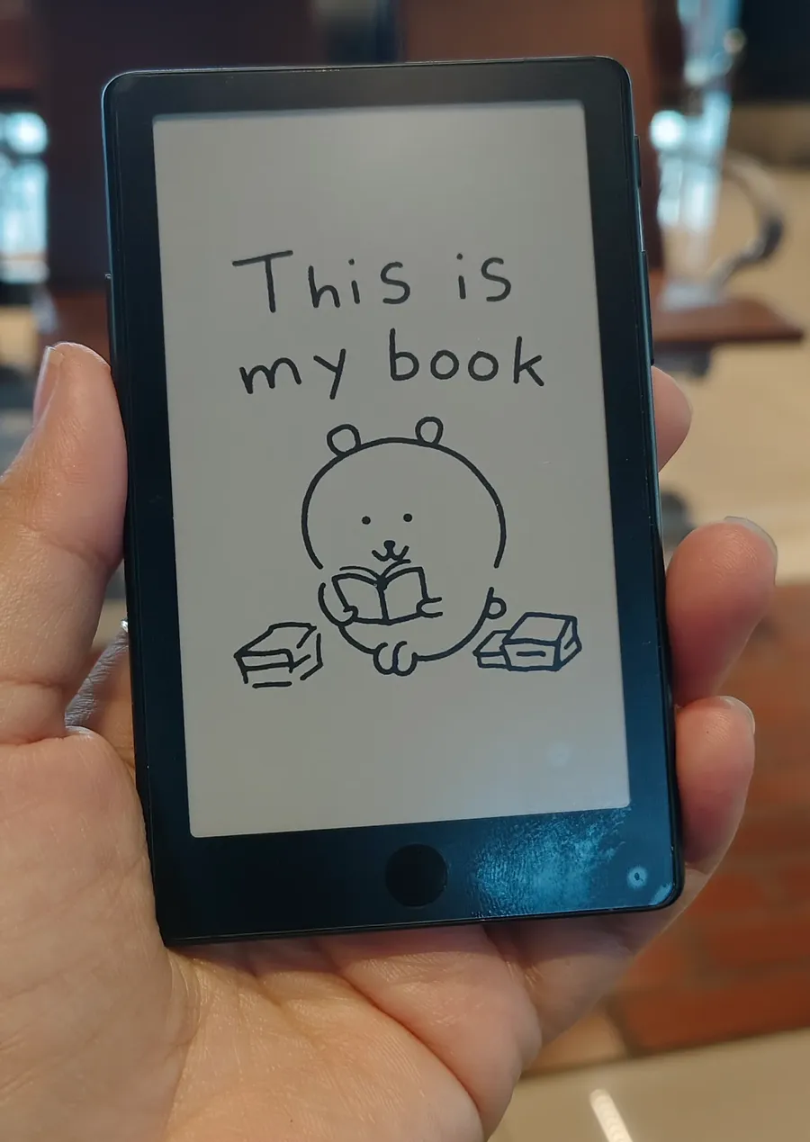 Xteink X4 Pro tenue à une main dans un salon d'aéroport, croquis affiché sur son écran e-ink