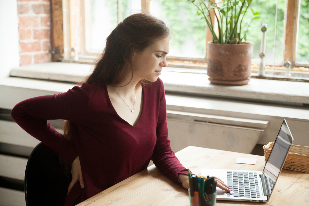 Femme assise à son bureau, la main dans les lombaires