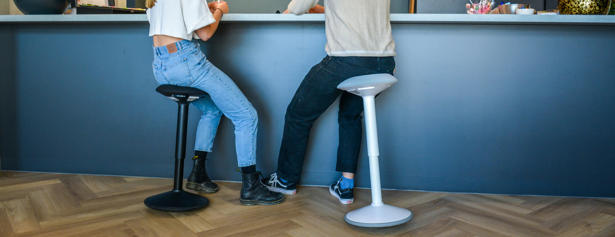 Deux personnes en assis-debout sur tabourets ergonomiques à un comptoir haut