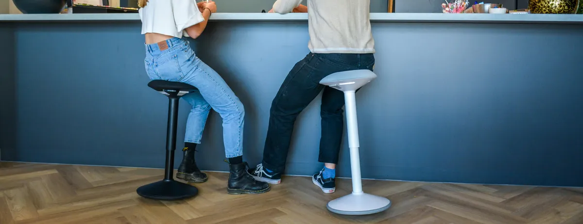Deux personnes en assis-debout sur tabourets ergonomiques à un comptoir haut