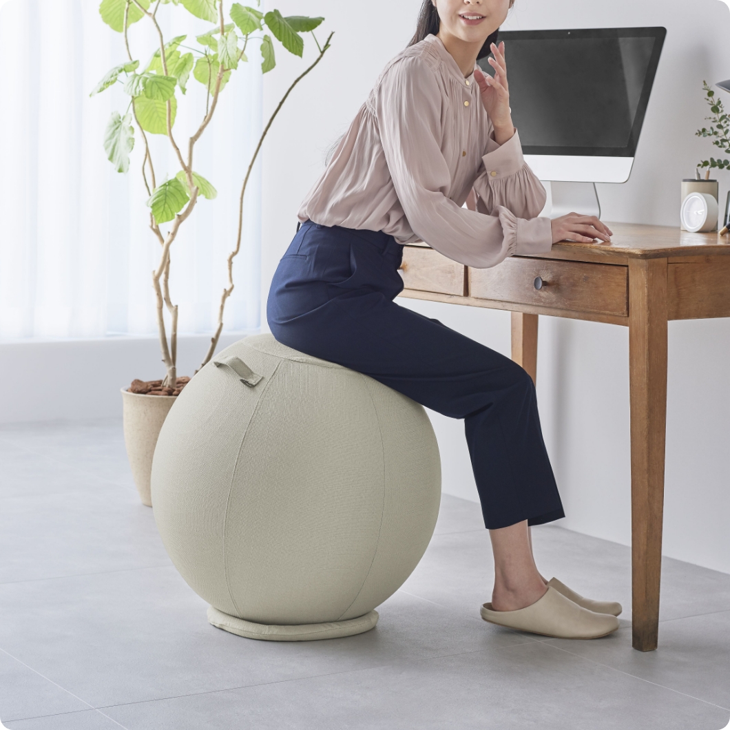 Femme assise sur un ballon ergonomique habillé devant un bureau en bois clair