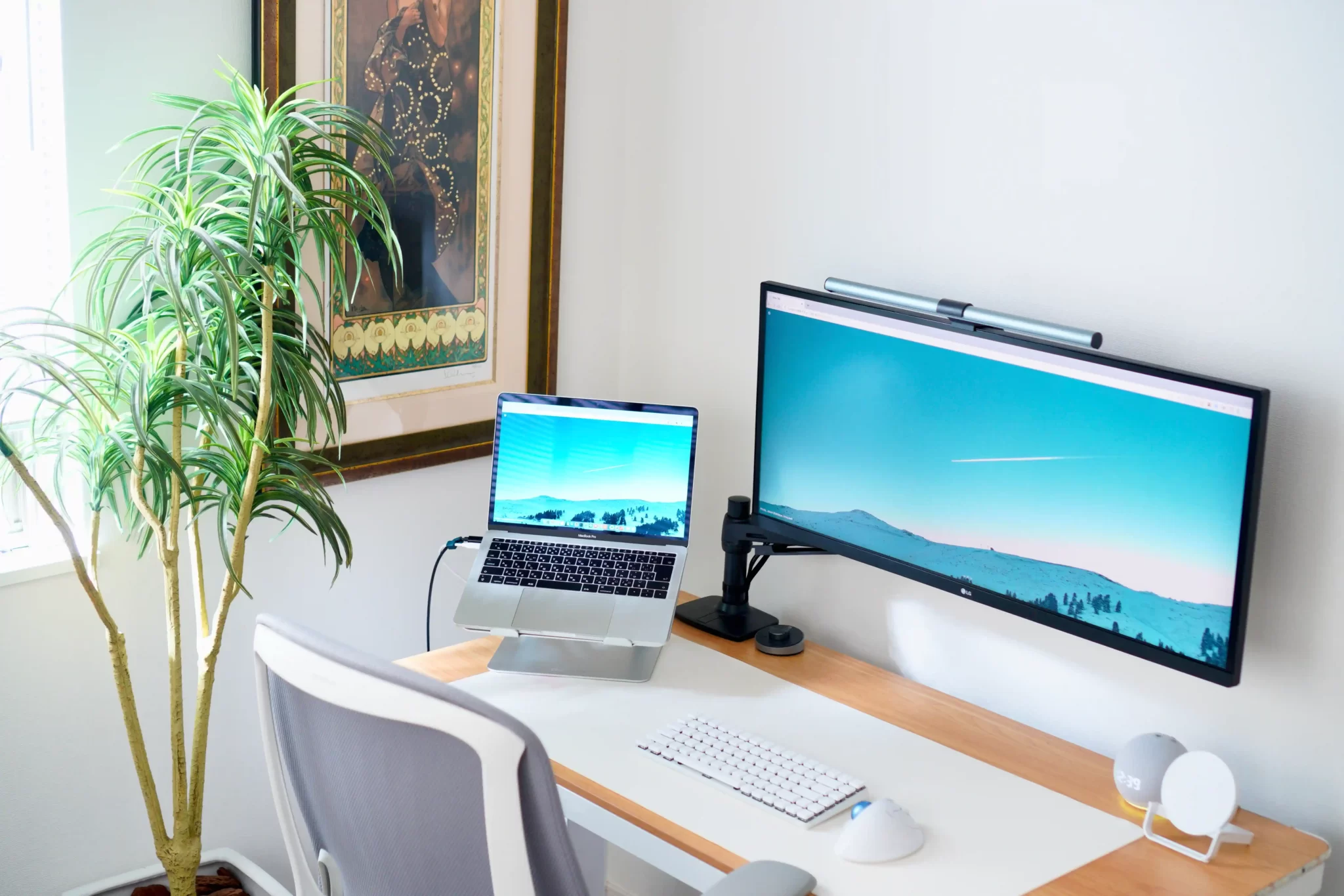 Écran ultrawide 34 pouces sur bras articulé à côté d'un MacBook