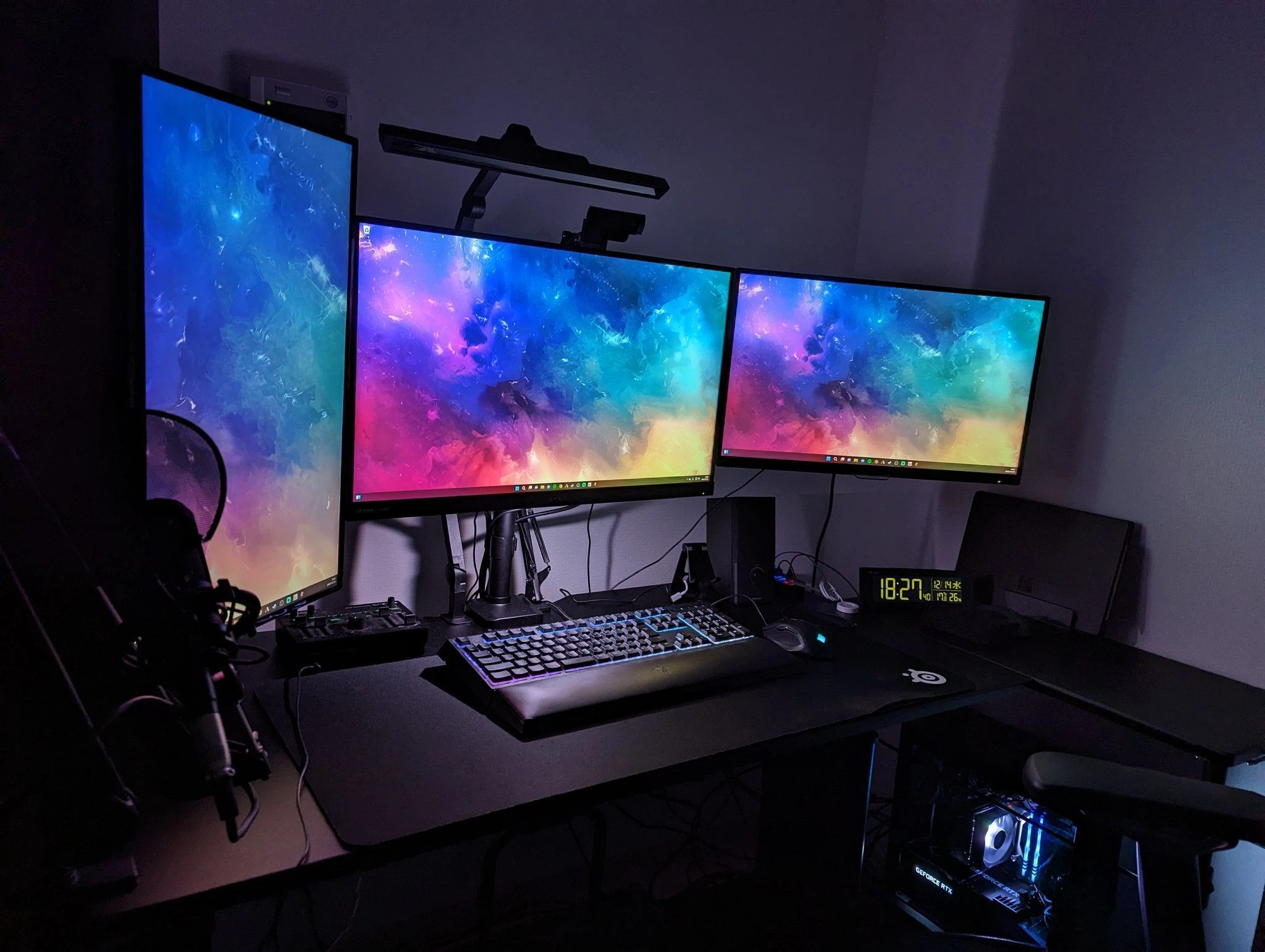 Setup gaming sombre avec plusieurs écrans aux fonds colorés et clavier RGB